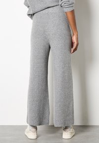 Pantaloni ampi in maglia waffle grigia con vita alta e texture morbida, abbinati a sneakers di colore chiaro.