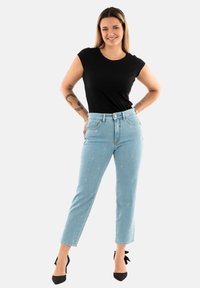 Jeans de mezclilla azul claro con patrones florales bordados, combinados con una camiseta negra ajustada y tacones negros. Diseño simple y ajustado.
