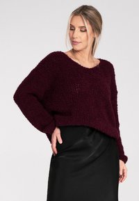 Bordowy, teksturowany sweter dzianinowy z szerokim dekoltem i luźnym krojem, w połączeniu z elegancką czarną spódnicą. Pozioma linia na dolnej części.