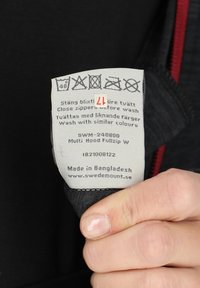 Clothing care label featuring washing instructions and symbols, predominantly gray with black lettering. Includes size "L" and manufacturing details.