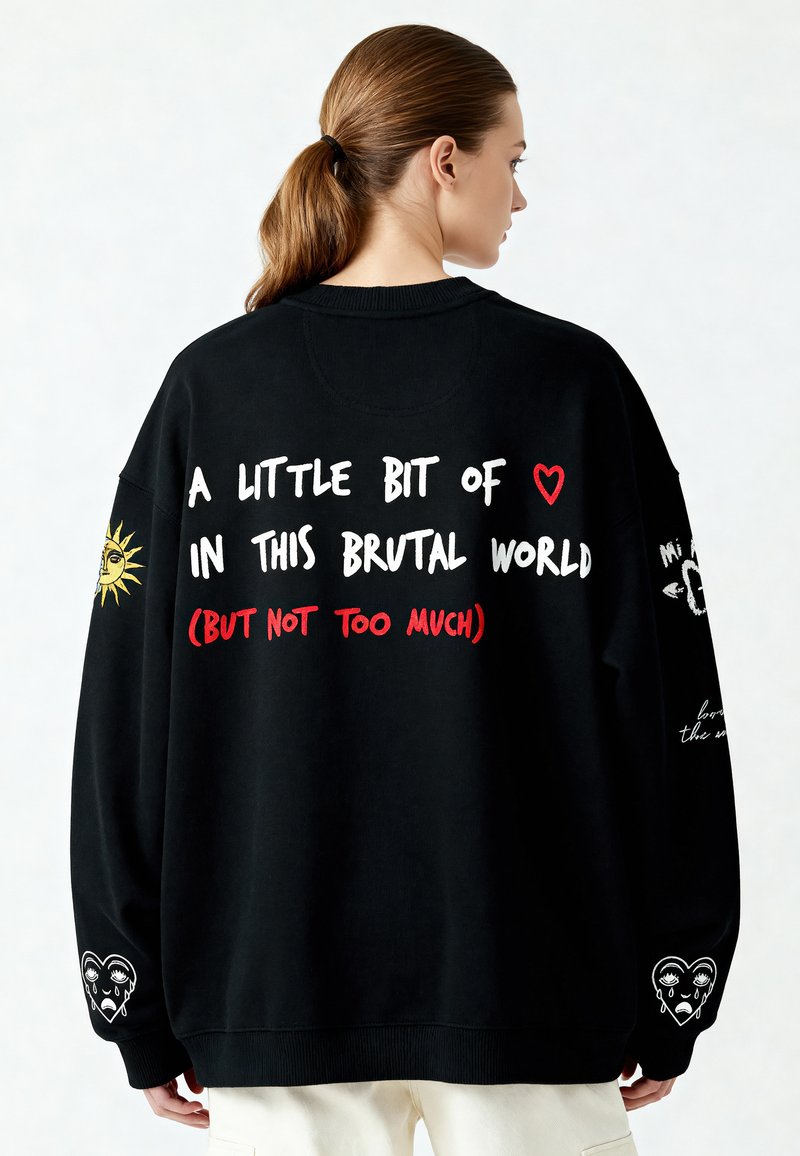 Černá oversized mikina s bílým a červeným textem na zádech, sluneční grafikou na jednom rukávu a designem srdce se slzami na druhém rukávu.
