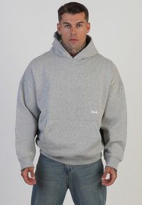 Felpa grigia realizzata in tessuto morbido, con una grande tasca frontale e un cappuccio regolabile. Marchio evidente nell'angolo in basso a sinistra.