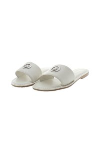 White leather slide sandals featuring a broad strap with a round metallic emblem and a flat, beige rubber sole. Smooth texture throughout.