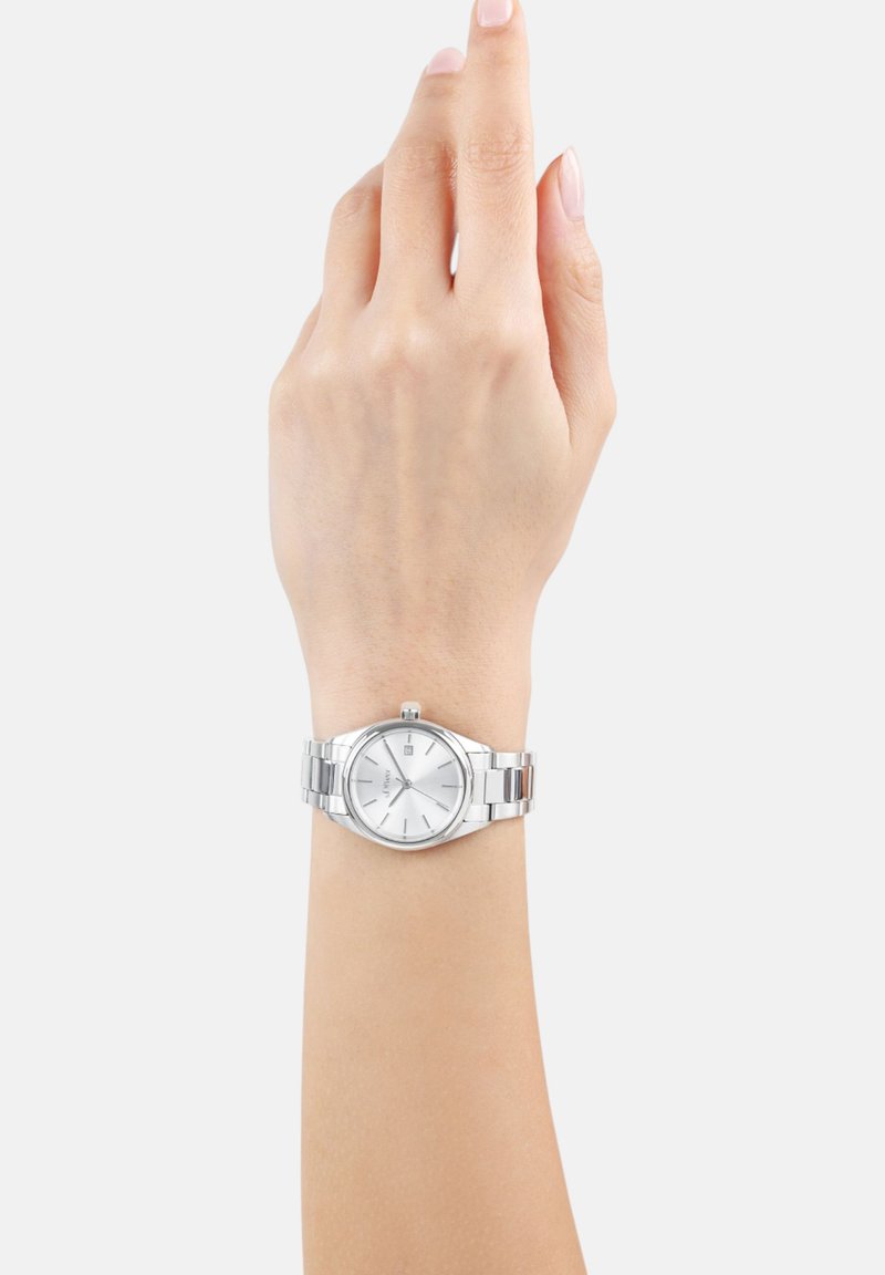 Zilveren polshorloge met een ronde wijzerplaat, witte wijzerplaat en een metalen band. Voorzien van minimalistische uurmarkeringen en een datumaanduiding op 3 uur.