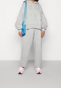 Grå sweatshirt och matchande byxor, båda gjorda av mjukt tyg. Blåaxelväska. Skorna har rosa accenter och svarta sulor.