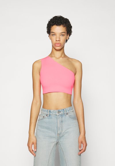 Rosa en-skulder crop topp i et elastisk stoff, med en tettsittende design. Brukt sammen med lyseblå høytlivsjeans som viser en midjeutskjæring.
