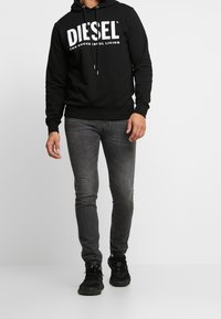 Black hoodie with white "DIESEL" logo, paired with dark grey slim-fit jeans and black athletic shoes. The hoodie features a drawstring hood.