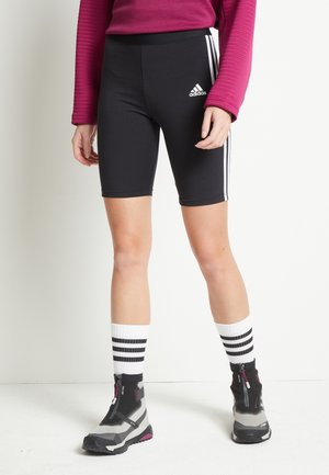 Zwarte fietsshorts met wit Adidas-logo en drie zijstrepen, gecombineerd met gestreepte sokken en grijze laarzen met ritsen.