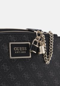 Czarna syntetyczna torebka z błyszczącą plakietką z logo, akcentami z łańcuszka oraz teksturowanym wzorem z subtelnym motywem marki. Zapięcie na zamek błyskawiczny.