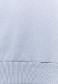 Sudadera azul claro hecha de un tejido suave, con una textura lisa y puños y dobladillo acanalados. Diseño simple sin patrones ni accesorios.
