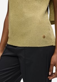 Guld ribbet strik-top med rund halsudskæring, med et lille cirkulært logo, samt parret med sorte skræddersyede bukser. Glat tekstur, afslappet pasform.