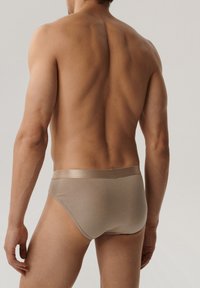 Beżowe męskie slipy o gładkiej fakturze, z satynowym pasem. Dopasowane do ciała, podkreślające kształt i kontury.