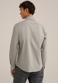 Chemise à manches longues gris clair avec un col classique, des poignets boutonnés et une texture lisse, vue de dos sur un fond neutre.