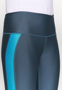 Legginsy z wysokim stanem w ciemnoniebieskim kolorze z jasnoniebieskim panelem bocznym, wykonane z gładkiego, elastycznego materiału o dopasowanym kroju i płaskich szwach.