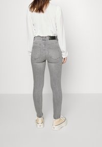 Jeans skinny de talle alto en gris con un acabado texturizado, que cuentan con bolsillos traseros y una cintura negra, combinados con una blusa blanca y zapatillas.