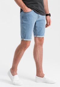 Vaaleansiniset farkkushortsit, joissa on käännetyt lahkeet, sivutaskut ja slim fit -muotoilu, yhdistettynä valkoisiin slip-on -kenkiin.