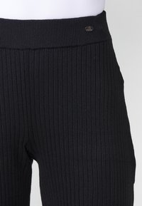 Leggings noirs à côtes présentant une large ceinture texturée avec un petit logo argenté. Le tissu a une texture douce et extensible.