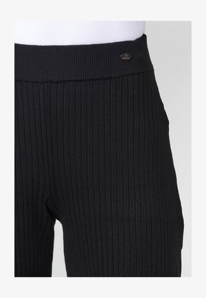 Mustad ribad leggings, mille laia tekstureeritud vöökoha ja väikese hõbedase logo aktsendiga. Kanga tekstuur on pehme ja veniv.