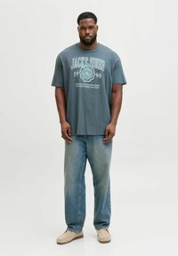 T-shirt in cotone grigio con testo grafico bold in bianco e azzurro chiaro. Abbinato a jeans a gamba larga in denim chiaro e scarpe slip-on beige.