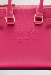 Sac à main fuchsia avec une surface texturée, présentant des quincailleries en or, des poignées doubles et un logo "LIU·JO MILANO" en relief à l'avant.