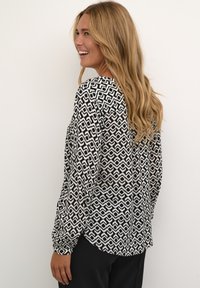 Blusa a maniche lunghe con un motivo geometrico bianco e nero, tessuto morbido, vestibilità rilassata e orlo arrotondato.