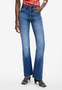 Höga, utsvängda jeans i medelblå denim med slitningsdetaljer, femficksdesign och kopparfärgad hårdvara.