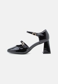 Black patent leather Mary Jane shoe with two adjustable buckled straps and a block heel on a white background.