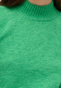 Pull en tricot de couleur verte claire avec un col côtelé haut. La texture est lisse avec un motif uniforme et sans coutures ni embellissements visibles.