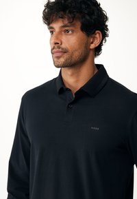 Zwarte lange mouwen polo met een zachte textuur, voorzien van een knoopsluiting kraag en een discreet geborduurd logo op de linkerborst.