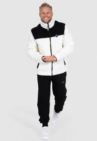 Herrfleecejacka, vit med svart övre del, hel dragkedja, hög krage, två framfickor. Kombinerad med svarta joggers och vita sneakers.