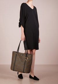 Svart V-ringad klänning med lätta ärmar, paired med en vävd svart och guldrandig tote-väska med svarta handtag och en guldaccent.