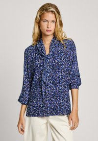 Blusa floreale blu con maniche lunghe, caratterizzata da un collo drappeggiato e una vestibilità ampia. Il tessuto ha una consistenza morbida e un motivo vivace.