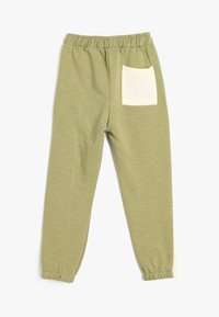 Pantalones de chándal verdes de algodón con una cintura elástica, piernas ajustadas y un bolsillo trasero de parche en crema que contrasta.