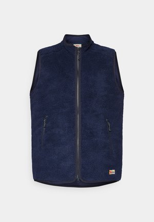 Jūras zilas krēpju veste ar augstu apkakli, priekšējo rāvējslēdzēju un divām sānu kabatām ar rāvējslēdzēju. Mīksta tekstūra un izolēts dizains siltumam.