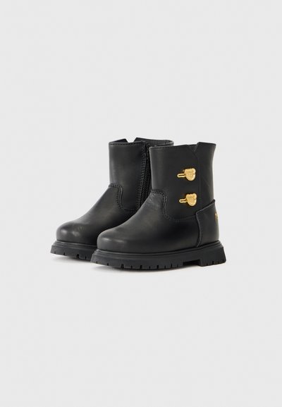 Botines de cuero negro con un acabado texturizado, que cuentan con una cremallera lateral y acentos de hardware dorado. Suela de goma negra con textura para mayor tracción.