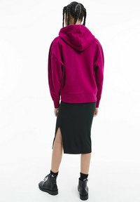 Fuchsia oversized hoodie med huva, tillsammans med en svart ribbad midiklänning med en sidöppning. Svarta kängor avslutar outfiten.