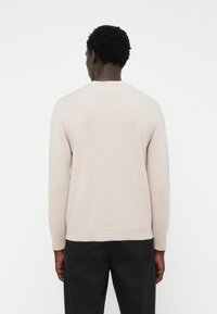 Suéter gris claro de material suave, con cuello redondo y mangas largas, con puños y dobladillo de canalé, llevado sobre pantalones oscuros.