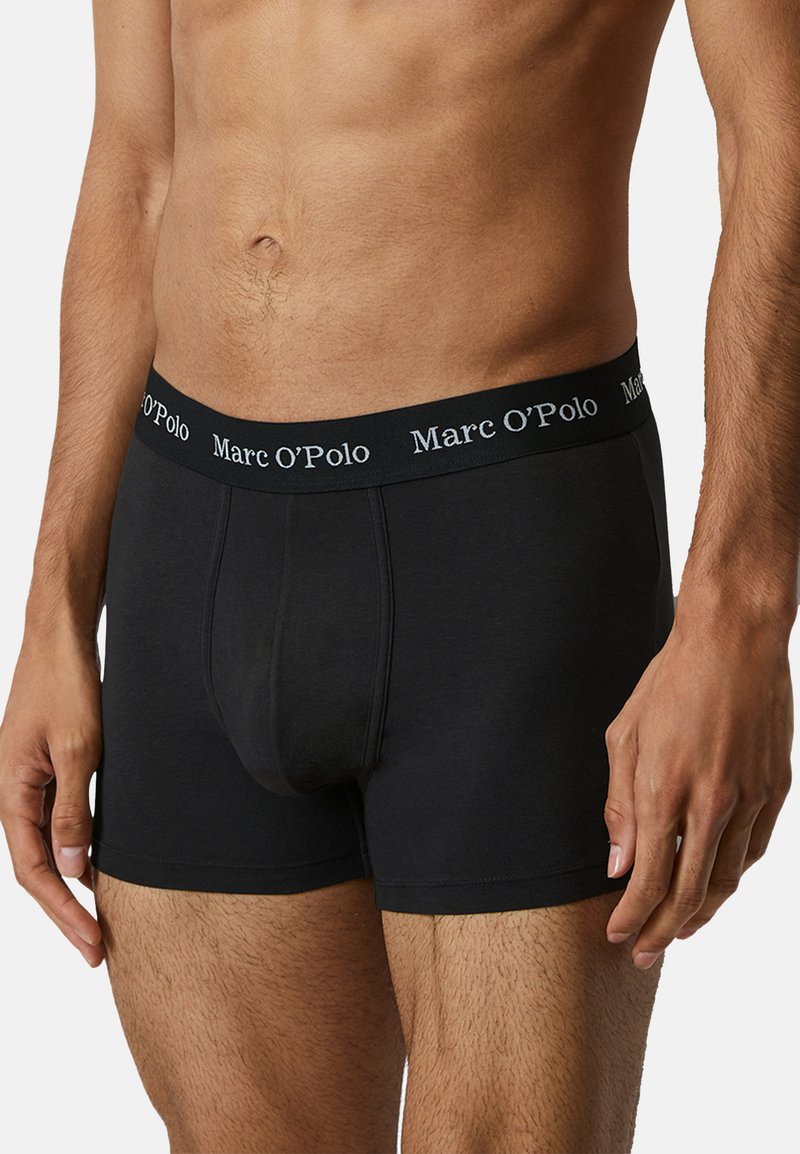 Musta bokserimalli, jossa on pehmeä kangas, tiukka istuvuus sekä leveä vyötärö, jossa on valkoinen "Marc O'Polo" -logo.