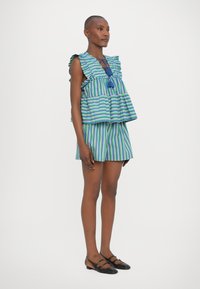 Top senza maniche a righe con spalline fluttuanti e scollatura con fiocco, abbinato a pantaloni corti a righe e scarpe nere piatte con cinturini.
