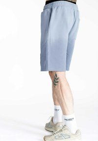 Lyseblå atletikshorts med elastisk talje, sidelommer og en glat overflade, kombineret med beige sneakers og hvide sokker.