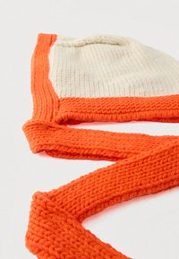 Kootud müts kreemja ja oranži tooniga. Omaduseks on tekstuuriga kudum, oranž riba ja paelad, mis pakuvad soojust ja reguleeritavat istuvust.