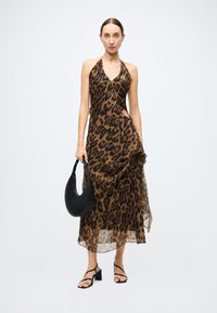 Robe à bretelles imprimé léopard au design fluide, tissu marron et noir, détail découpe latérale. Le mannequin tient un sac noir et porte des talons à lanières.