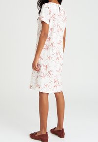 Weißes Kleid mit rosa floralem Muster, kurze Ärmel, knielang, weicher Stoff, Rückenschlitz-Detail, kombiniert mit kastanienbraunen Ballerinas.