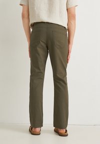 Pantalones de algodón verdes con corte recto, bolsillos traseros y trabillas para el cinturón, combinados con sandalias marrones. Diseño simple y funcional.