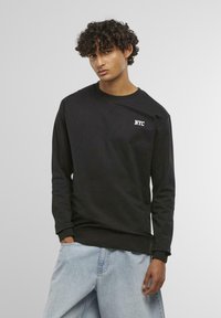 Felpa nera in cotone, con scollo rotondo e maniche lunghe. Logo "NYC" stampato in bianco sul petto. Shorts in denim.