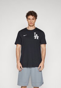 Black Nike t-shirt with "LA" logo in white on the left chest. Short sleeves, round neckline, made of cotton. Gray athletic shorts visible below.
