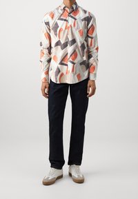 Camicia con maniche lunghe e bottoni, caratterizzata da un motivo astratto multicolore in rosso, grigio e beige. Abbinata a jeans scuri e scarpe da tennis bianche casual.