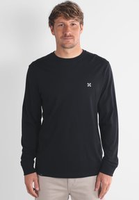 Camiseta de manga larga negra, de material de algodón, con cuello redondo, que presenta un pequeño logo blanco en el pecho y un corte relajado.