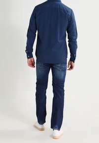 Tummansininen painonappipaita kauluksella, yhdistetty tummansinisiin farkkuihin ja valkoisiin lenkkareihin, esittelee rentoa ja hyvin istuvaa muotoilua.