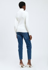Maglione bianco a collo alto a coste abbinato a jeans in denim blu; l'outfit presenta una siluetta aderente e un design semplice.